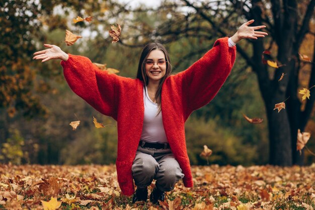 Giovane bella donna che cammina nella sosta di autunno e che tiene le foglie