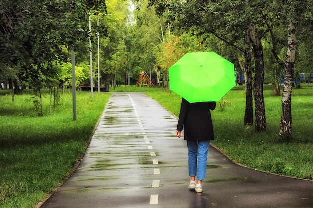 Giovane bella donna che cammina sotto un ombrello verde