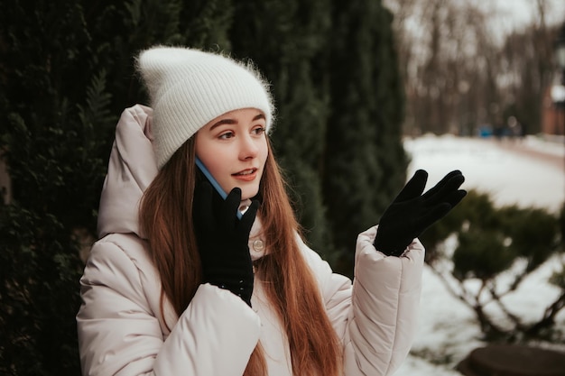 Giovane bella donna che celebra giacca calda vestita, in piedi vicino all'albero di Natale, parlando al telefono