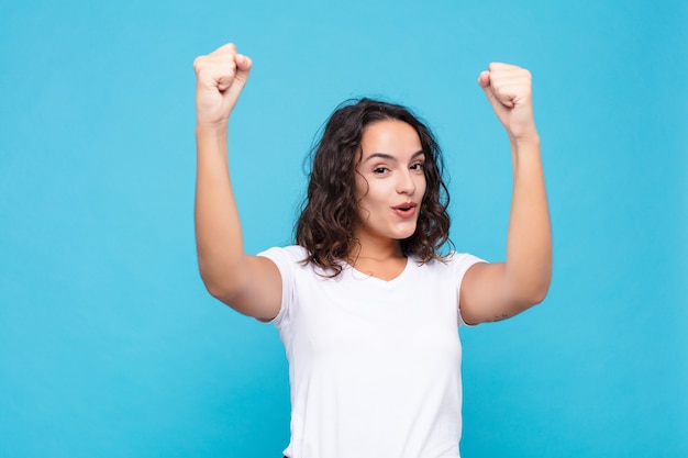 Giovane bella donna che celebra un incredibile successo come una vincitrice, che sembra entusiasta e felice di dire che prendilo! contro il muro blu