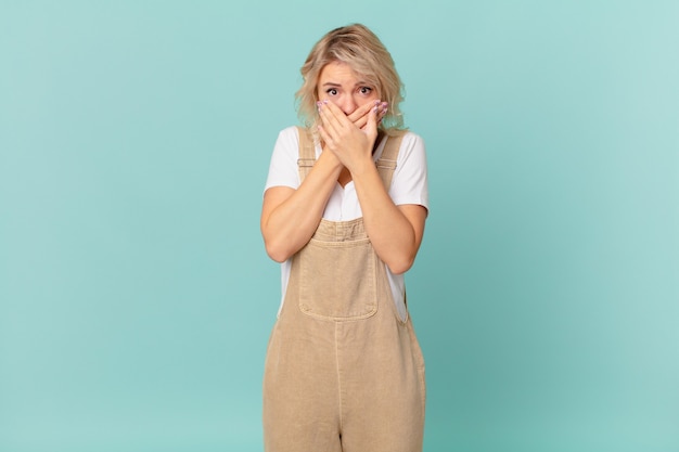 Giovane bella donna che copre la bocca con le mani con uno shock