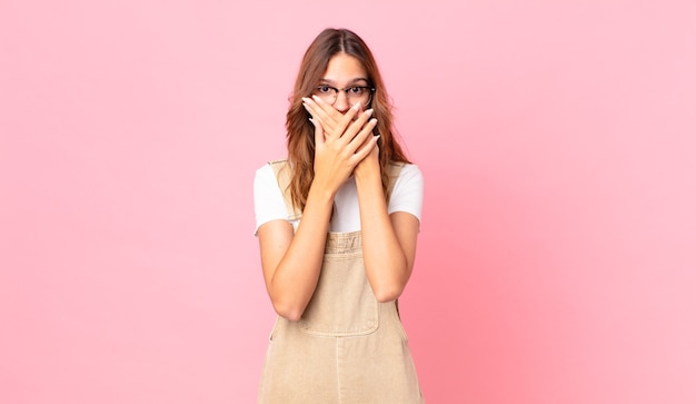 Giovane bella donna che copre la bocca con le mani con uno shock