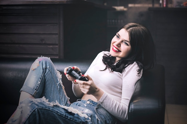 Giovane bella donna che gioca un gioco per console sul divano sexy e alla moda