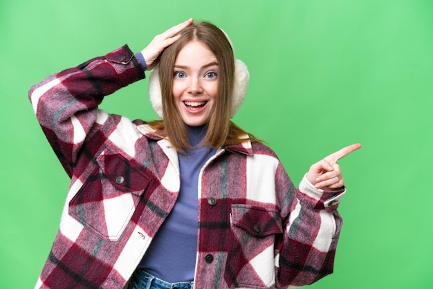 Giovane bella donna che indossa manicotti invernali su sfondo chroma key isolato sorpreso e puntando il dito di lato