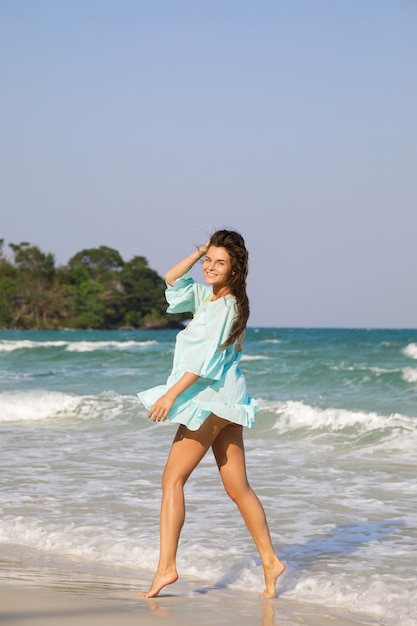 Giovane bella donna che indossa un bel vestito blu sta camminando in riva al mare