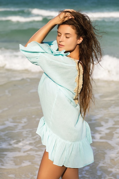 Giovane bella donna che indossa un bel vestito blu sta camminando in riva al mare