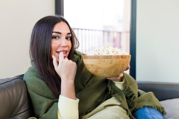 Giovane bella donna che mangia popcorn seduto su un divano a casa