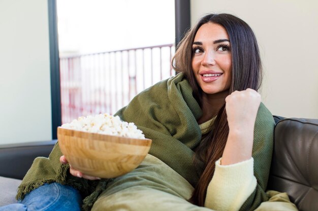 Giovane bella donna che mangia popcorn seduto su un divano a casa