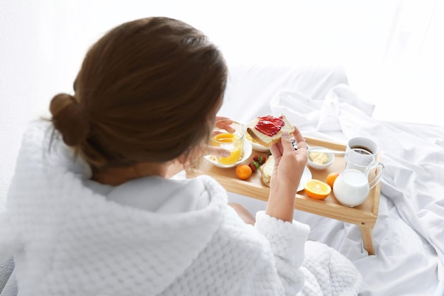 Giovane bella donna che mangia prima colazione sul letto