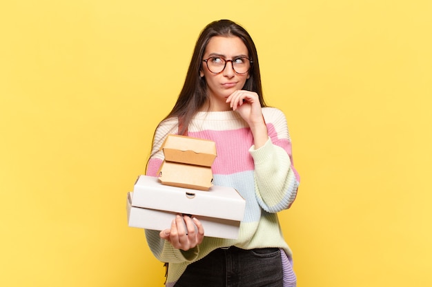 Giovane bella donna che pensa, si sente dubbiosa e confusa, con diverse opzioni, chiedendosi quale decisione prendere. prendi un concetto di fast food