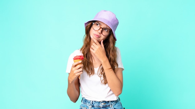 Giovane bella donna che pensa, si sente dubbiosa e confusa con in mano un gelato. concetto di estate