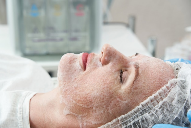 Giovane bella donna che riceve trattamenti nei saloni di bellezza con schiuma detergente per il viso facial