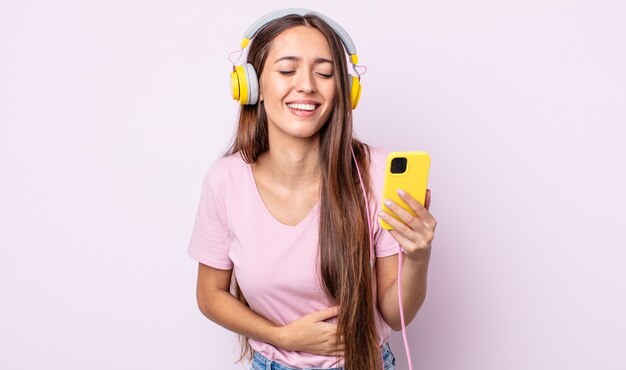 Giovane bella donna che ride ad alta voce per qualche scherzo esilarante. cuffie e smartphone