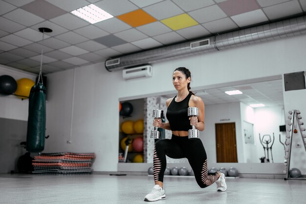 Giovane bella donna che risolve con i dumbbells in ginnastica.