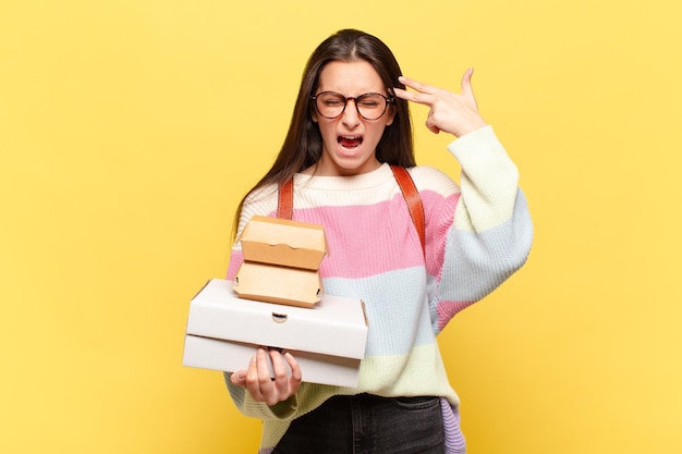 Giovane bella donna che sembra infelice e stressata, gesto suicida che fa il segno della pistola con la mano, indicando la testa. prendi un concetto di fast food