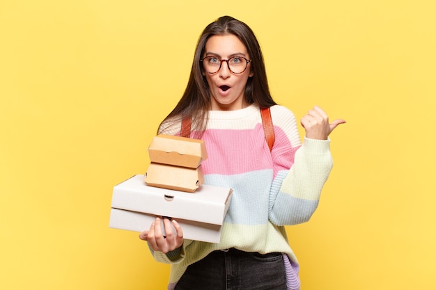 Giovane bella donna che sembra stupita per l'incredulità, indicando un oggetto sul lato e dicendo wow, incredibile. prendi un concetto di fast food