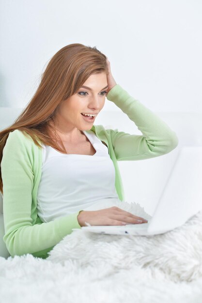 Giovane bella donna che si rilassa a letto a casa, usando il laptop