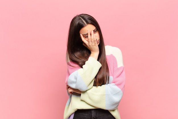 Giovane bella donna che si sente annoiata, frustrata e assonnata dopo un compito noioso, noioso e noioso, tenendo il viso con la mano