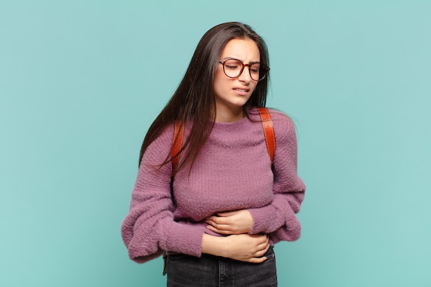 Giovane bella donna che si sente ansiosa, malata, malata e infelice, soffre di un doloroso mal di stomaco o influenza. concetto di studente