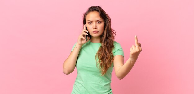 Giovane bella donna che si sente arrabbiata, infastidita, ribelle e aggressiva e tiene in mano uno smartphone