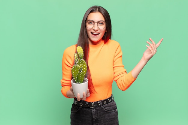 Giovane bella donna che si sente felice, sorpresa e allegra, sorridente con atteggiamento positivo, realizzando una soluzione o un'idea. cactus