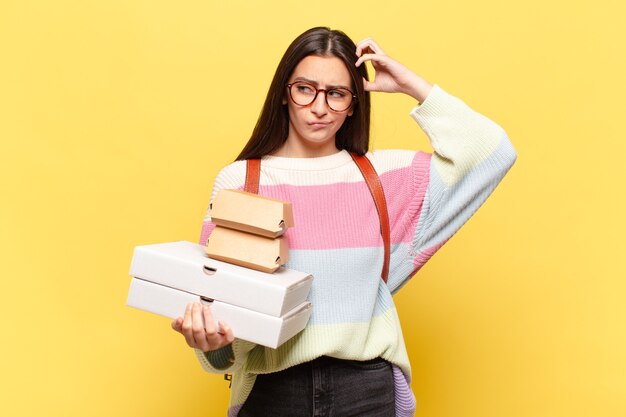 Giovane bella donna che si sente perplessa e confusa, si gratta la testa e guarda di lato. prendi un concetto di fast food