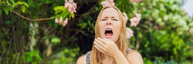 Giovane bella donna che soffia il naso davanti all'albero in fiore primavera concetto di allergia banner formato lungo