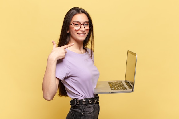 Giovane bella donna che sorride con sicurezza indicando il proprio ampio sorriso, atteggiamento positivo, rilassato e soddisfatto