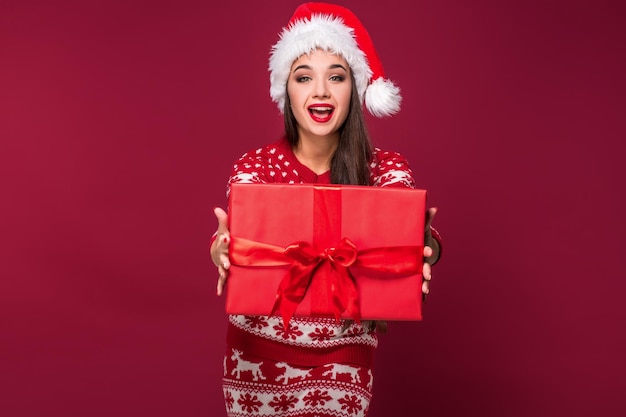 Giovane bella donna che tiene il regalo di Natale nelle sue mani sullo sfondo rosso dello studio