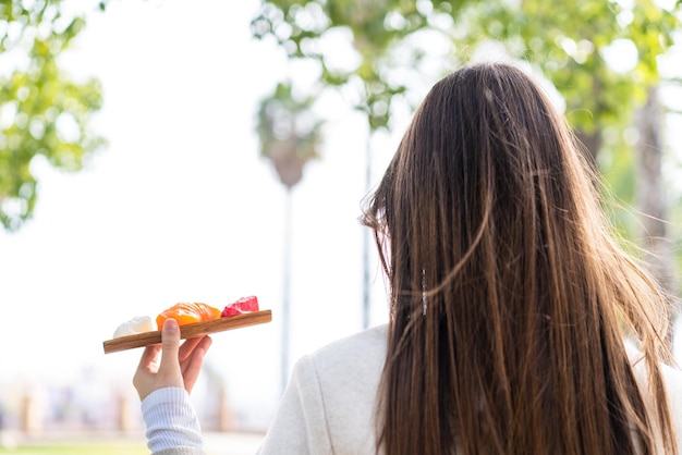 Giovane bella donna che tiene il sashimi all'aperto in posizione arretrata