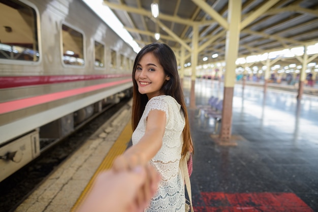 Giovane bella donna che tiene la mano dell'uomo nella stazione ferroviaria