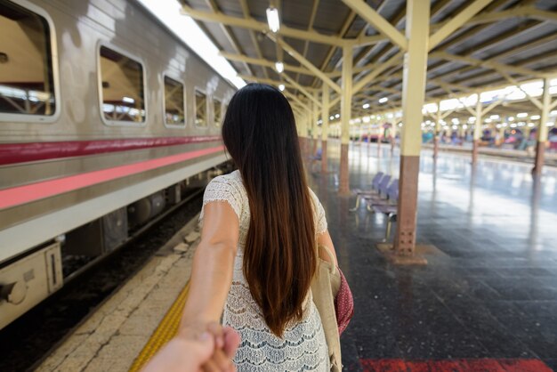 Giovane bella donna che tiene la mano dell'uomo nella stazione ferroviaria