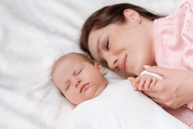 Giovane bella donna che tiene la piccola mano della sua bambina addormentata in camera da letto