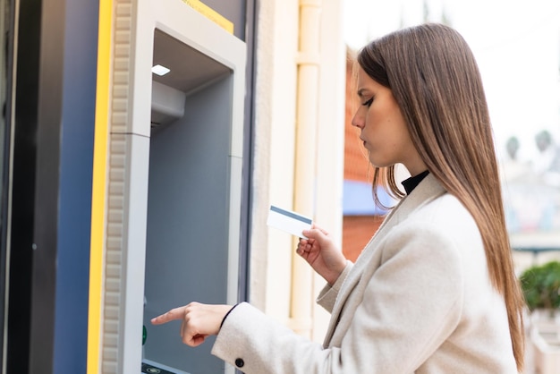 Giovane bella donna che utilizza un bancomat