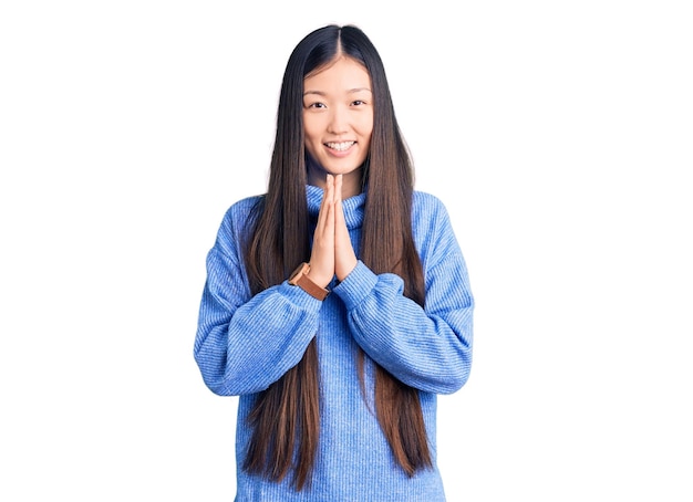 Giovane bella donna cinese che indossa un maglione dolcevita casual che prega con le mani insieme chiedendo perdono sorridendo fiducioso.