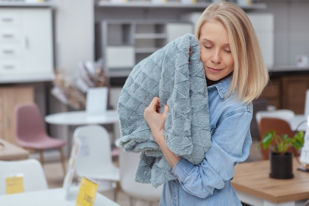 Giovane bella donna coccole per una soffice coperta, shopping per articoli per la casa al negozio di arredamento