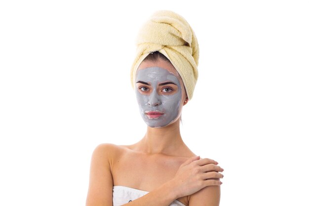 Giovane bella donna con asciugamano giallo sulla testa e maschera cosmetica blu che le tocca il viso