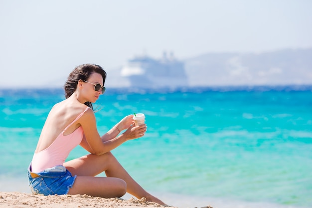 Giovane bella donna con caffè sulla spiaggia durante la vacanza tropicale. La ragazza si gode il wekeend su una delle bellissime spiagge di Mykonos, in Grecia, in Europa.