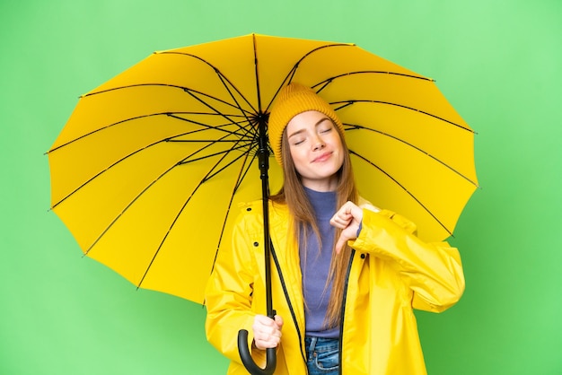 Giovane bella donna con cappotto antipioggia e ombrello su sfondo chroma key isolato orgoglioso e soddisfatto di sé