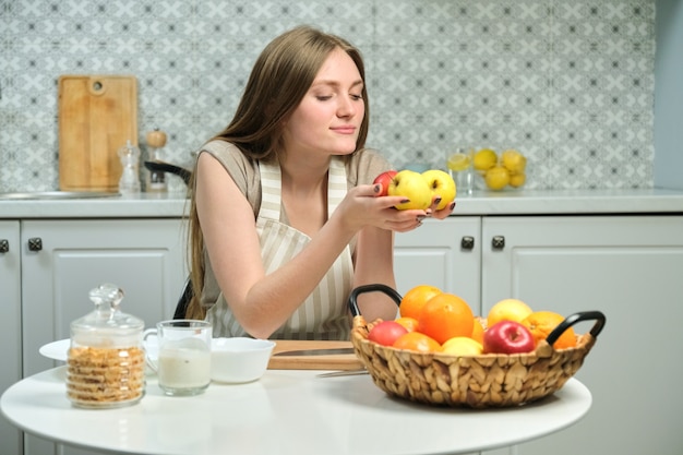 Giovane bella donna con frutta in cucina, donna seduta al tavolo e che tiene le mele nelle sue mani