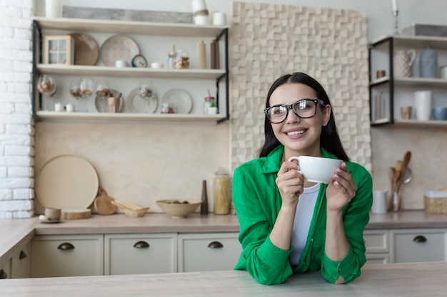 Giovane bella donna con gli occhiali e una camicia casual verde a casa in cucina guarda la webcam