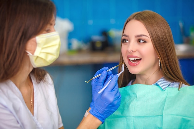 Giovane bella donna con i bei denti bianchi che si siedono su una sedia dentaria.