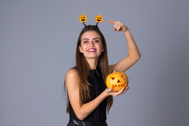 Giovane bella donna con i capelli lunghi in vestito nero che tiene una zucca e che indica la sua fascia