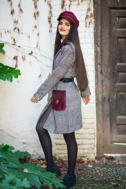 Giovane bella donna con il cappotto e il cappuccio d'uso di inverno dei capelli molto lunghi nel fondo delle foglie di autunno