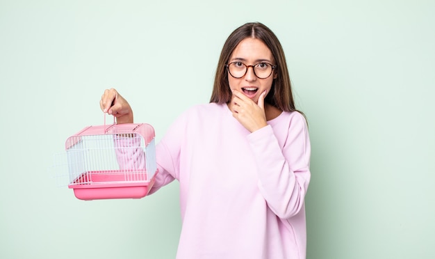 giovane bella donna con la bocca e gli occhi spalancati e la mano sul mento. concetto di gabbia per animali domestici