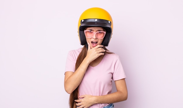 giovane bella donna con la bocca e gli occhi spalancati e la mano sul mento. motociclista e casco