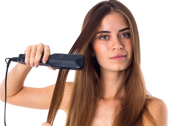 Giovane bella donna con lunghi capelli castani con piastra per capelli su sfondo bianco in studio