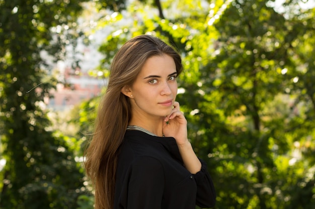 Giovane bella donna con lunghi capelli castani e collana d'argento in piedi indietro e che si fissa i capelli