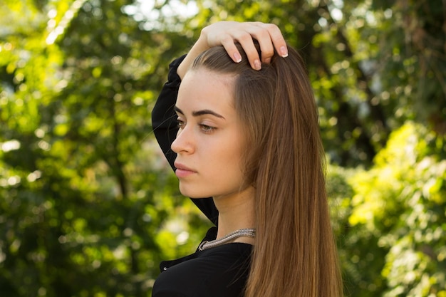 Giovane bella donna con lunghi capelli castani in camicetta nera e collana d'argento in piedi indietro