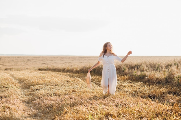 Giovane bella donna con lunghi capelli ricci pone in un campo di grano in estate al tramonto